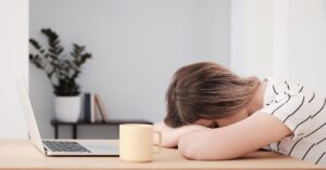 Abschalten nach der Arbeit ist nicht leicht, daher liegt Frau erschöpft am Schreibtisch