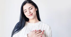 Frau hält mit meinen Händen ihre Herzgegen fest und lächelt. Sie praktiziert Selbstfürsorge